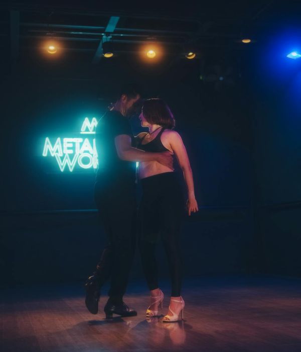 Woman performing a fluid cardio movement in a dark studio with cyan light.